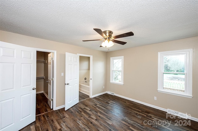 unfurnished bedroom with a walk in closet, a textured ceiling, ceiling fan, dark hardwood / wood-style floors, and a closet