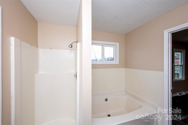 bathroom with a textured ceiling and shower with separate bathtub