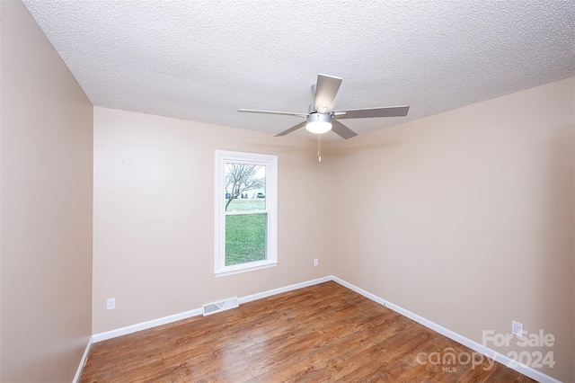 empty room with ceiling fan, wood-type flooring, and a textured ceiling