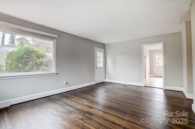 spare room featuring a textured ceiling, dark hardwood / wood-style flooring, and a healthy amount of sunlight