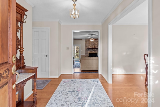 entryway featuring a fireplace, light wood-type flooring, ceiling fan with notable chandelier, and crown molding