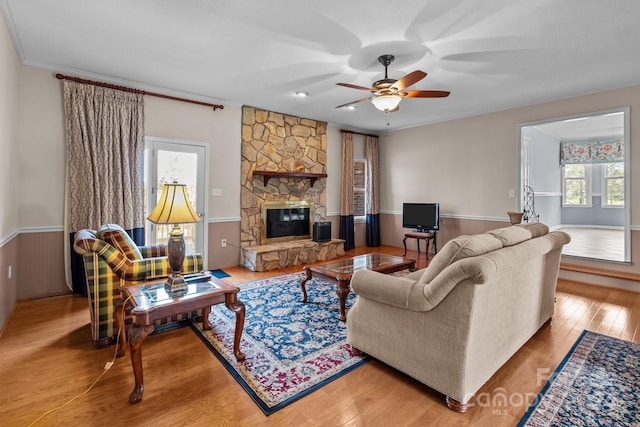 living room featuring a stone fireplace, ceiling fan, hardwood / wood-style floors, and crown molding