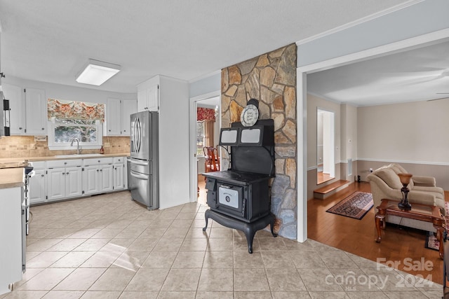 kitchen featuring sink, a wood stove, white cabinetry, stainless steel refrigerator, and light tile patterned flooring