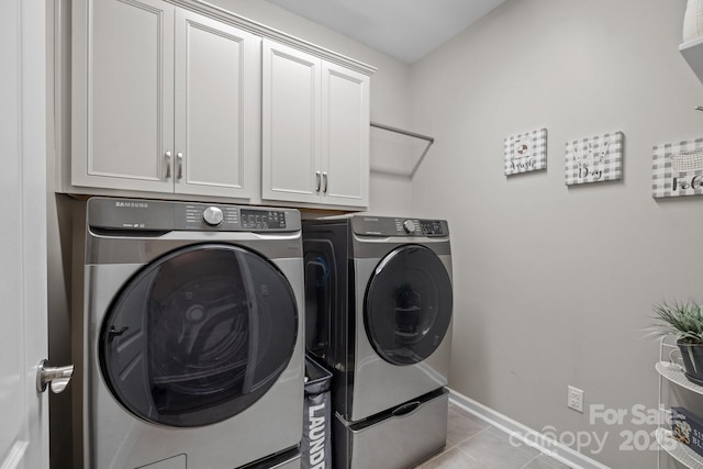 laundry room with washer and clothes dryer, light tile patterned flooring, and cabinets