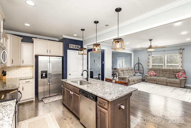 kitchen with ceiling fan, sink, stainless steel appliances, decorative light fixtures, and a center island with sink