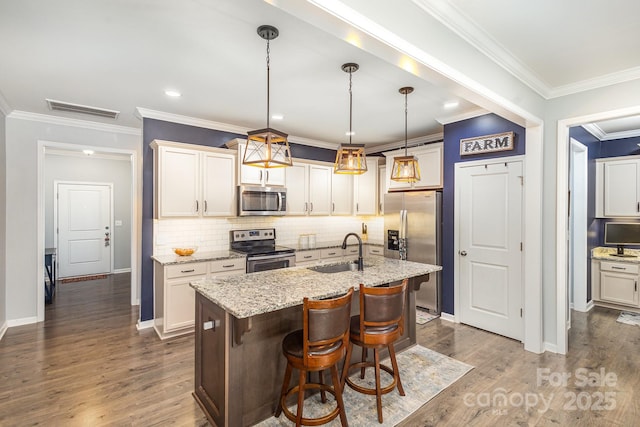 kitchen featuring decorative light fixtures, sink, stainless steel appliances, and an island with sink