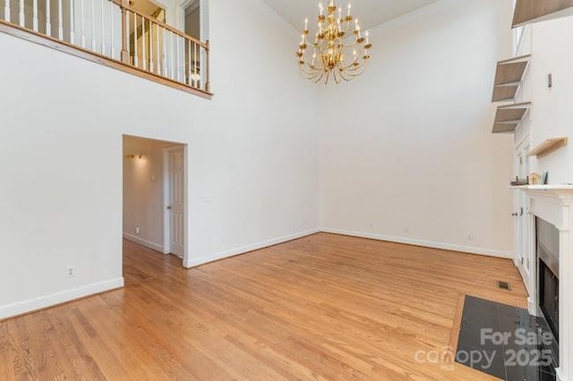 unfurnished living room featuring a notable chandelier, light hardwood / wood-style floors, and a high ceiling