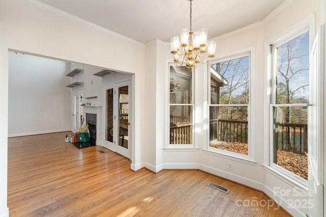 unfurnished dining area with ornamental molding, a healthy amount of sunlight, light wood-type flooring, and an inviting chandelier