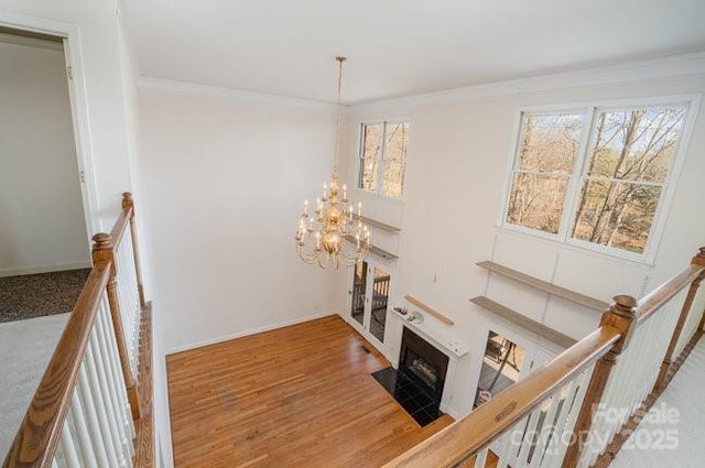 staircase with a fireplace, hardwood / wood-style flooring, an inviting chandelier, and crown molding