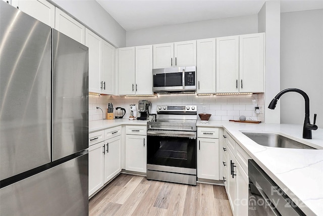 kitchen featuring sink, light hardwood / wood-style flooring, white cabinetry, stainless steel appliances, and light stone counters