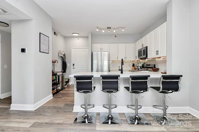 kitchen with white cabinetry, backsplash, a kitchen breakfast bar, kitchen peninsula, and stainless steel appliances