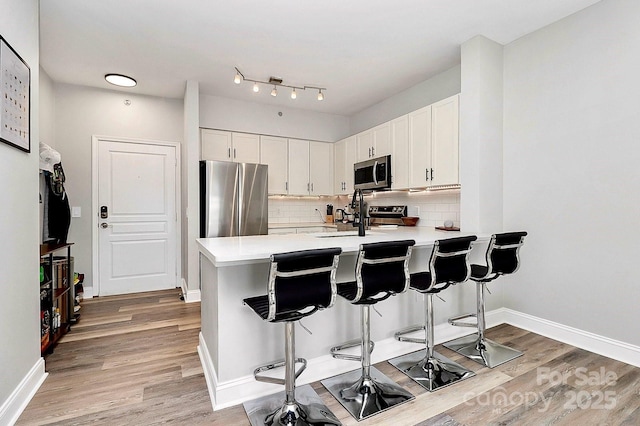 kitchen featuring appliances with stainless steel finishes, a kitchen bar, kitchen peninsula, and white cabinets