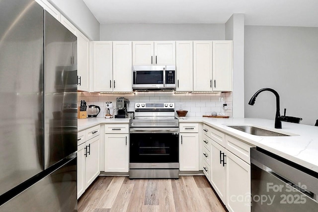 kitchen featuring sink, stainless steel appliances, light stone counters, white cabinets, and light wood-type flooring