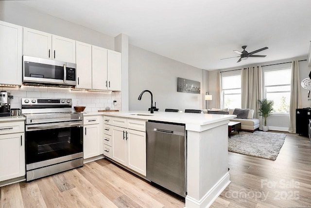 kitchen featuring sink, kitchen peninsula, white cabinets, and appliances with stainless steel finishes