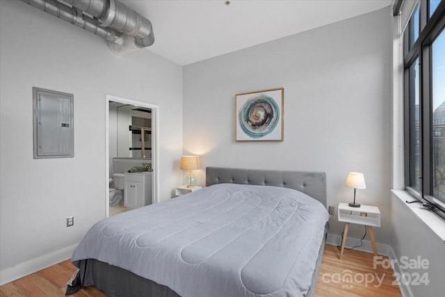 bedroom with connected bathroom, electric panel, and light hardwood / wood-style floors