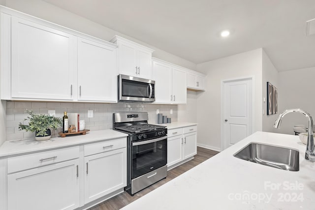 kitchen featuring appliances with stainless steel finishes, tasteful backsplash, dark wood-type flooring, sink, and white cabinetry