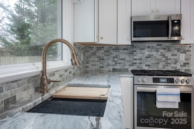 kitchen with light stone countertops, white cabinetry, sink, and appliances with stainless steel finishes