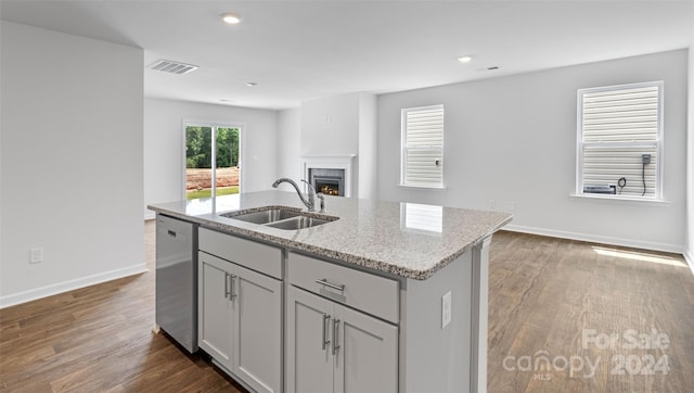 kitchen with light stone countertops, dark wood-type flooring, sink, dishwasher, and an island with sink