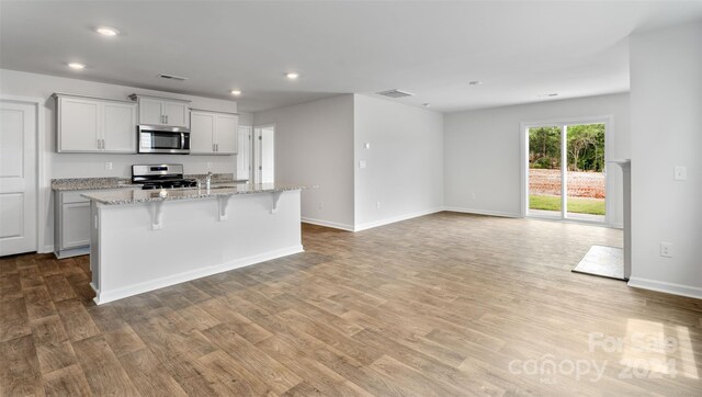 kitchen with a kitchen breakfast bar, light stone counters, stainless steel appliances, light hardwood / wood-style floors, and an island with sink