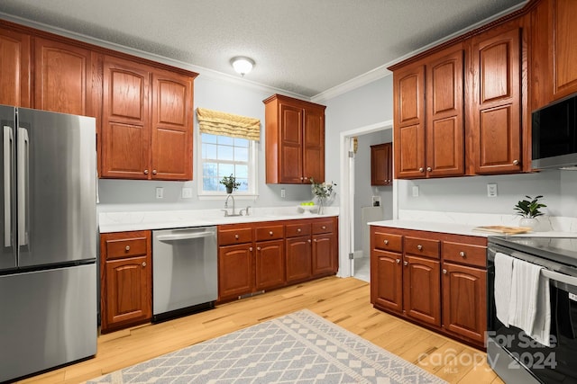 kitchen featuring ornamental molding, a textured ceiling, stainless steel appliances, sink, and light hardwood / wood-style floors