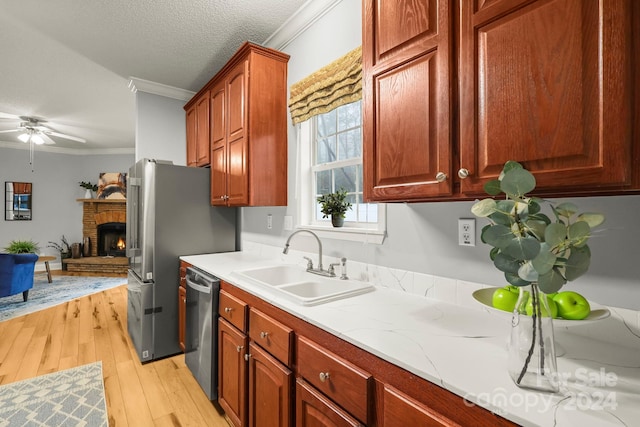 kitchen featuring a brick fireplace, stainless steel dishwasher, ornamental molding, a textured ceiling, and sink