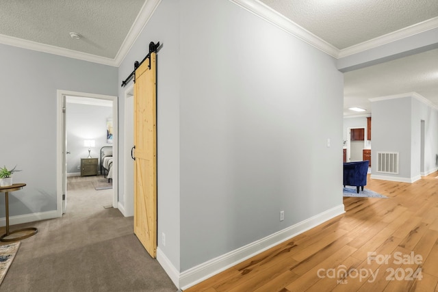 corridor with a barn door, crown molding, and a textured ceiling