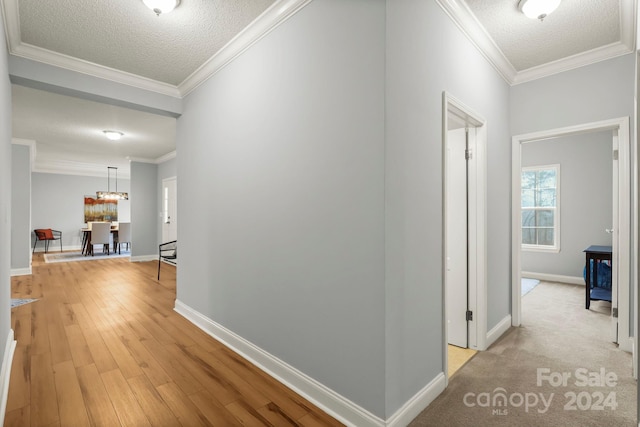 hall with light hardwood / wood-style floors, a textured ceiling, and ornamental molding