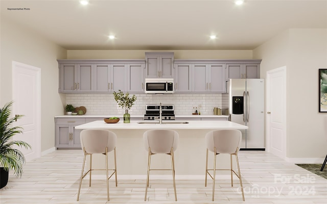 kitchen with gray cabinetry, a kitchen island with sink, sink, and appliances with stainless steel finishes