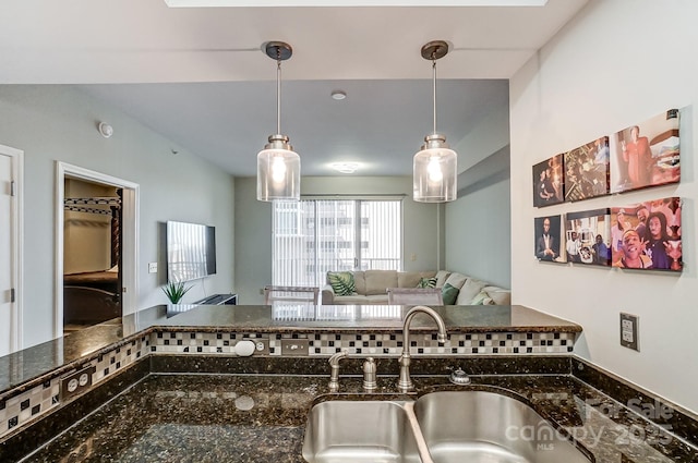 kitchen with decorative backsplash, dark stone counters, open floor plan, pendant lighting, and a sink