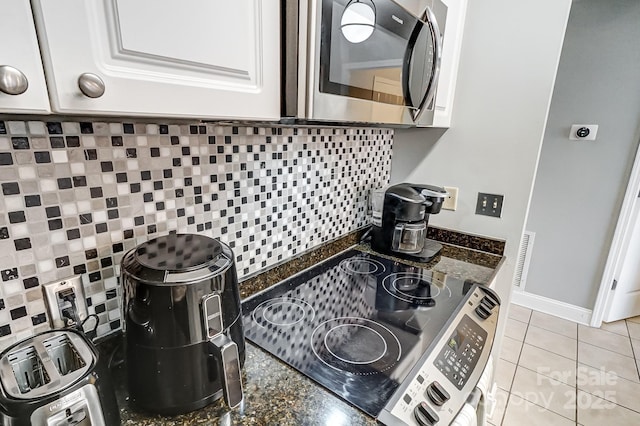 kitchen with light tile patterned floors, tasteful backsplash, stainless steel microwave, visible vents, and white cabinets