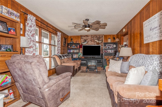 carpeted living room with a textured ceiling, a wood stove, ceiling fan, and wooden walls