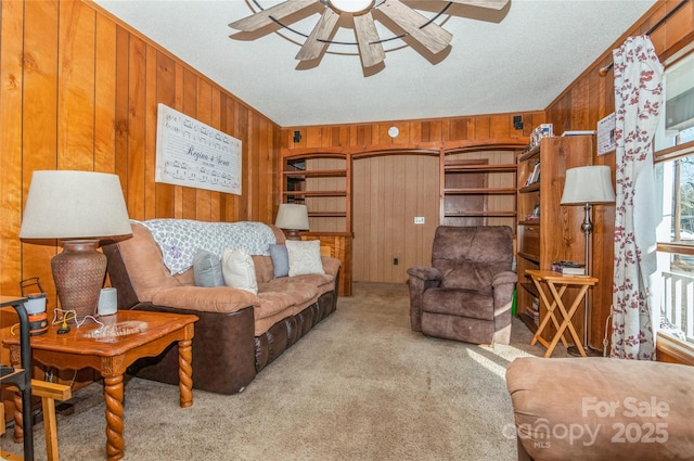 living room featuring ceiling fan, light colored carpet, a textured ceiling, and wooden walls