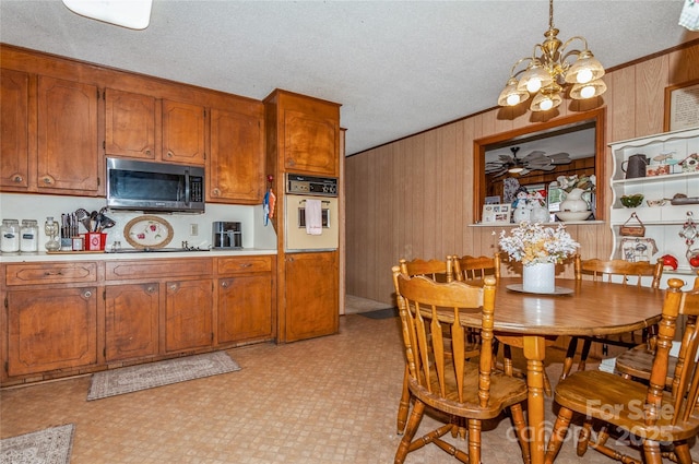 kitchen with ceiling fan with notable chandelier, decorative light fixtures, electric cooktop, oven, and wood walls