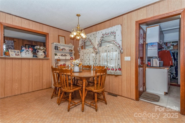 dining area featuring a notable chandelier, crown molding, a textured ceiling, and wooden walls