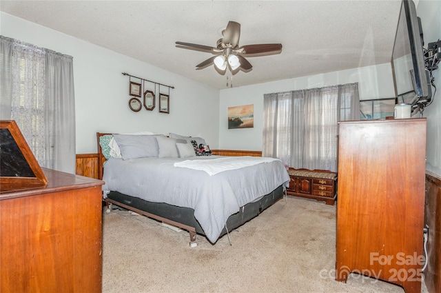 bedroom with ceiling fan, wooden walls, light carpet, and a textured ceiling