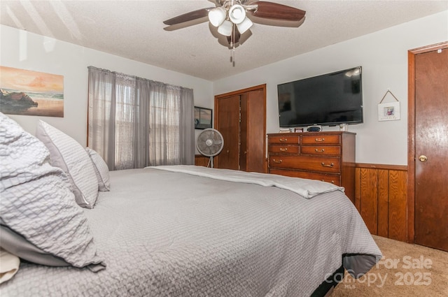 bedroom with a textured ceiling, ceiling fan, wooden walls, carpet floors, and a closet