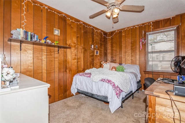 carpeted bedroom featuring a textured ceiling, ceiling fan, and wood walls