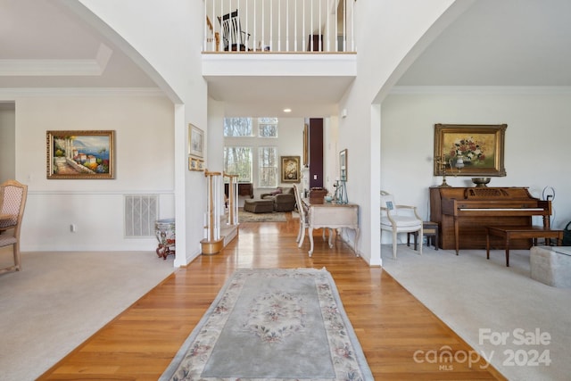 foyer with hardwood / wood-style floors, a towering ceiling, and crown molding