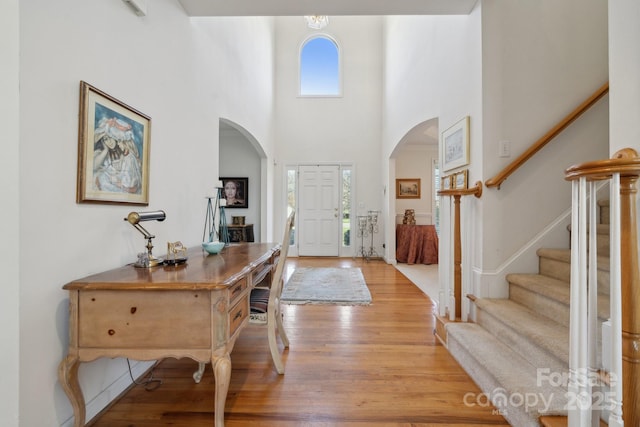 entryway featuring light wood-type flooring, a high ceiling, stairway, and arched walkways