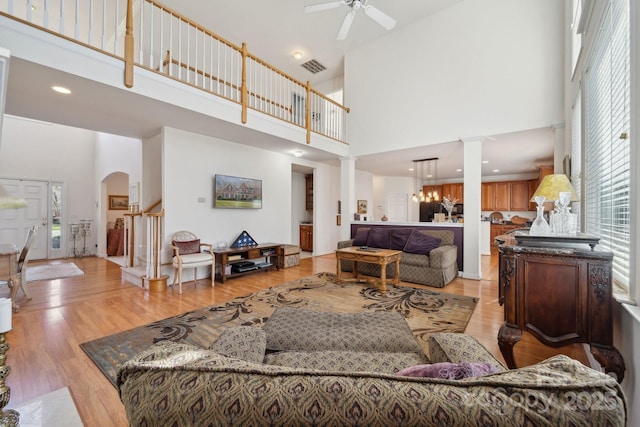 living area featuring decorative columns, visible vents, arched walkways, a high ceiling, and light wood-type flooring