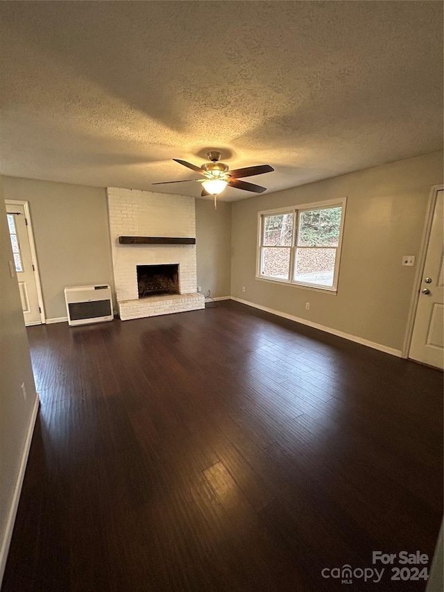 unfurnished living room featuring a brick fireplace, ceiling fan, a textured ceiling, dark hardwood / wood-style flooring, and heating unit