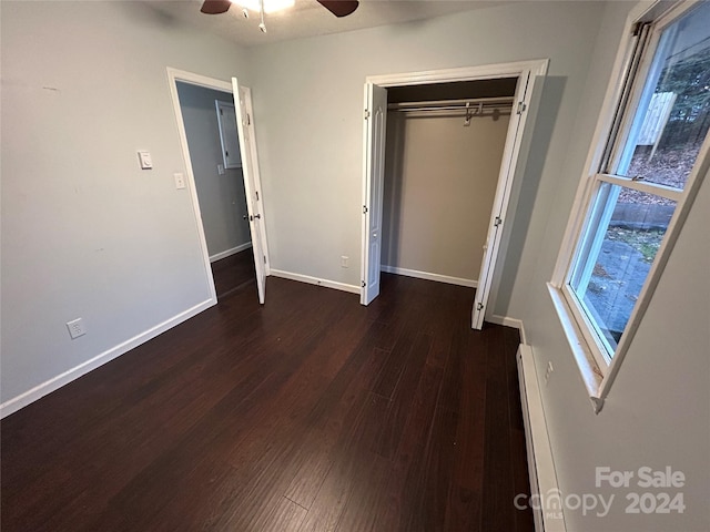 unfurnished bedroom featuring ceiling fan, dark hardwood / wood-style flooring, baseboard heating, and a closet