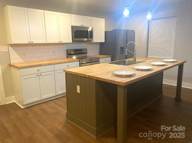 kitchen featuring hanging light fixtures, a kitchen island with sink, appliances with stainless steel finishes, and wooden counters