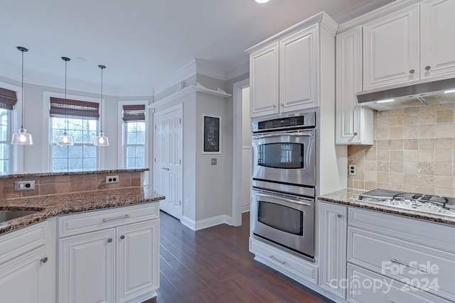 kitchen with tasteful backsplash, stainless steel appliances, decorative light fixtures, dark stone countertops, and white cabinetry