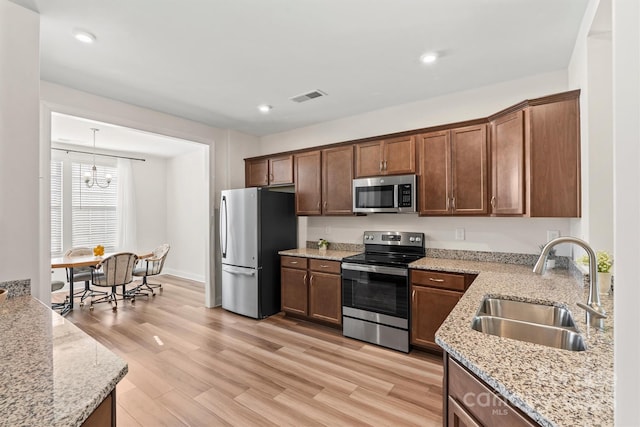 kitchen with stainless steel appliances, light stone countertops, pendant lighting, sink, and light hardwood / wood-style flooring