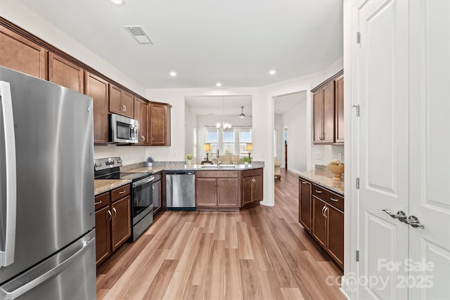 kitchen with stainless steel appliances, a notable chandelier, pendant lighting, light stone counters, and sink