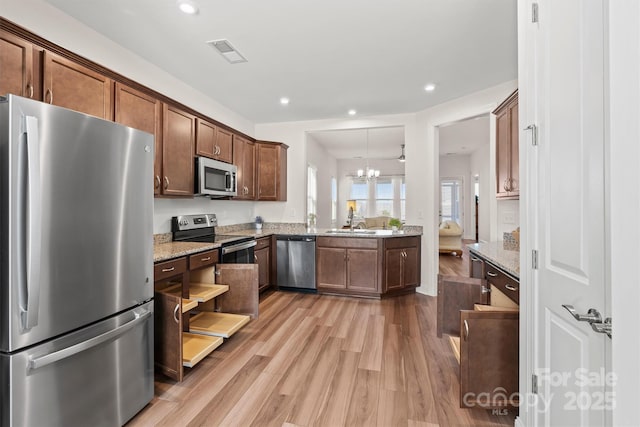 kitchen with light stone counters, a notable chandelier, light wood-type flooring, appliances with stainless steel finishes, and sink