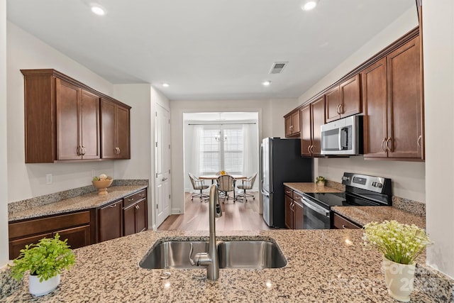 kitchen featuring light stone counters, stainless steel appliances, light wood-type flooring, and sink