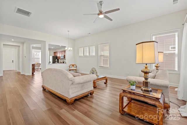 living room featuring ceiling fan with notable chandelier and light wood-type flooring