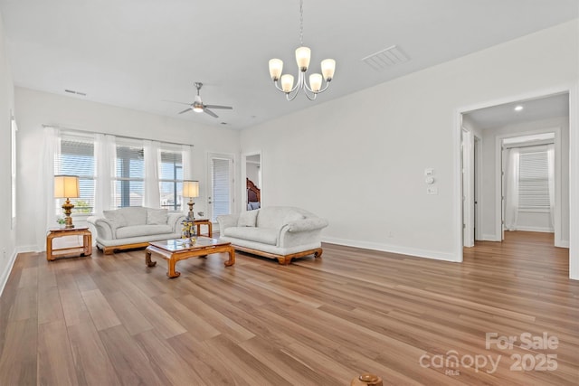 living room featuring ceiling fan with notable chandelier and light hardwood / wood-style flooring